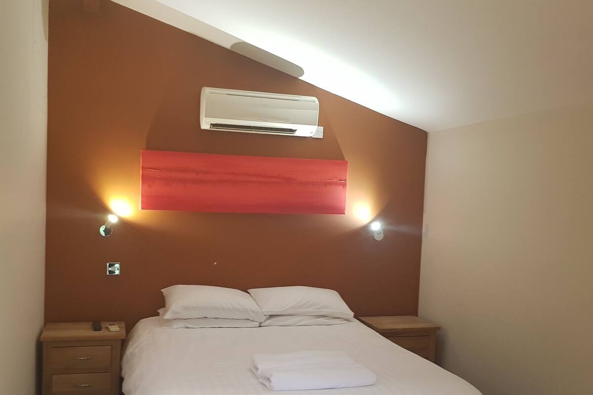 Een slaapkamer met een bed, twee nachtkastjes, een airconditioning en wandlampen.