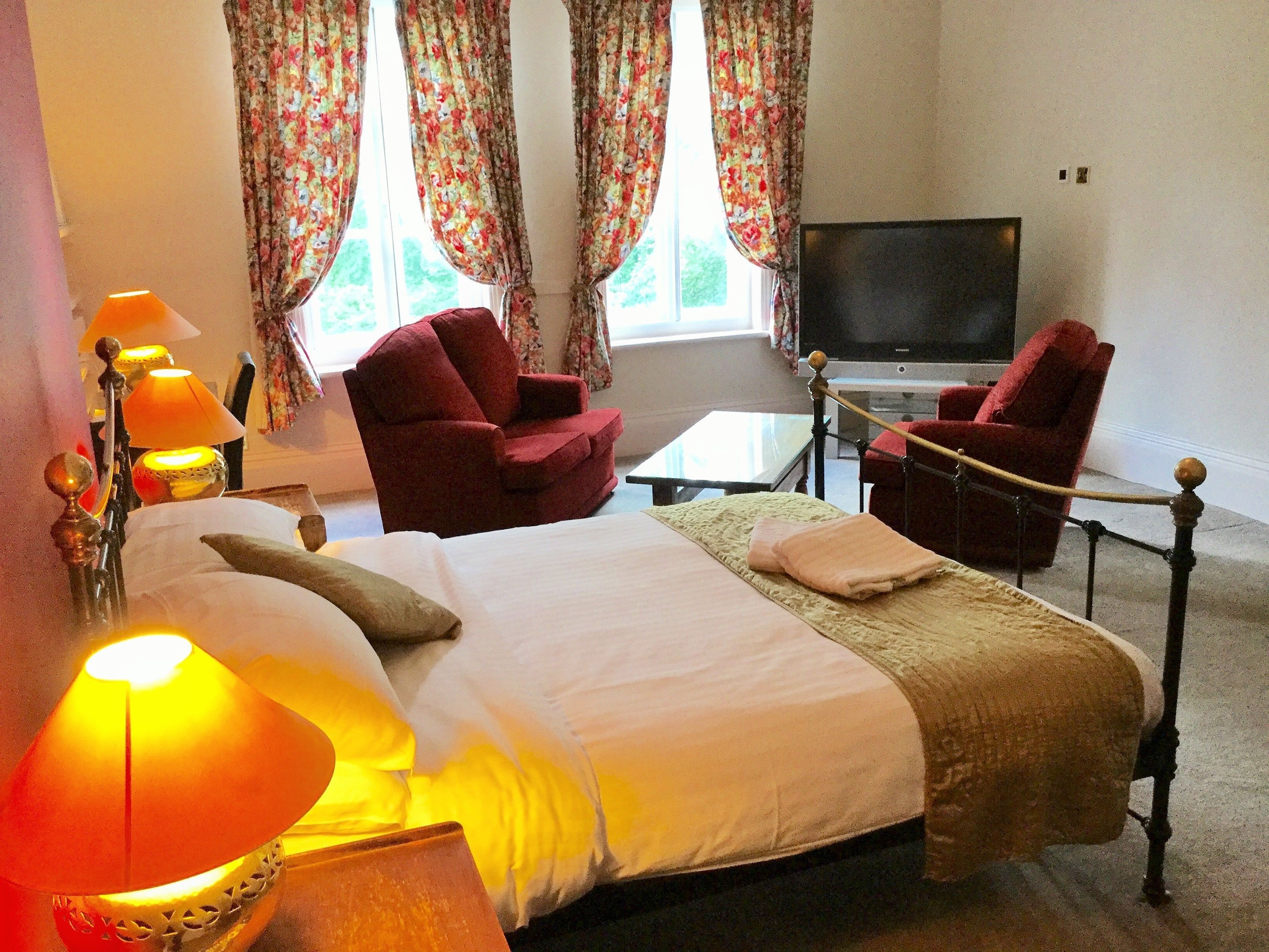 A hotel room with a bed, two armchairs, a TV, and a lamp.