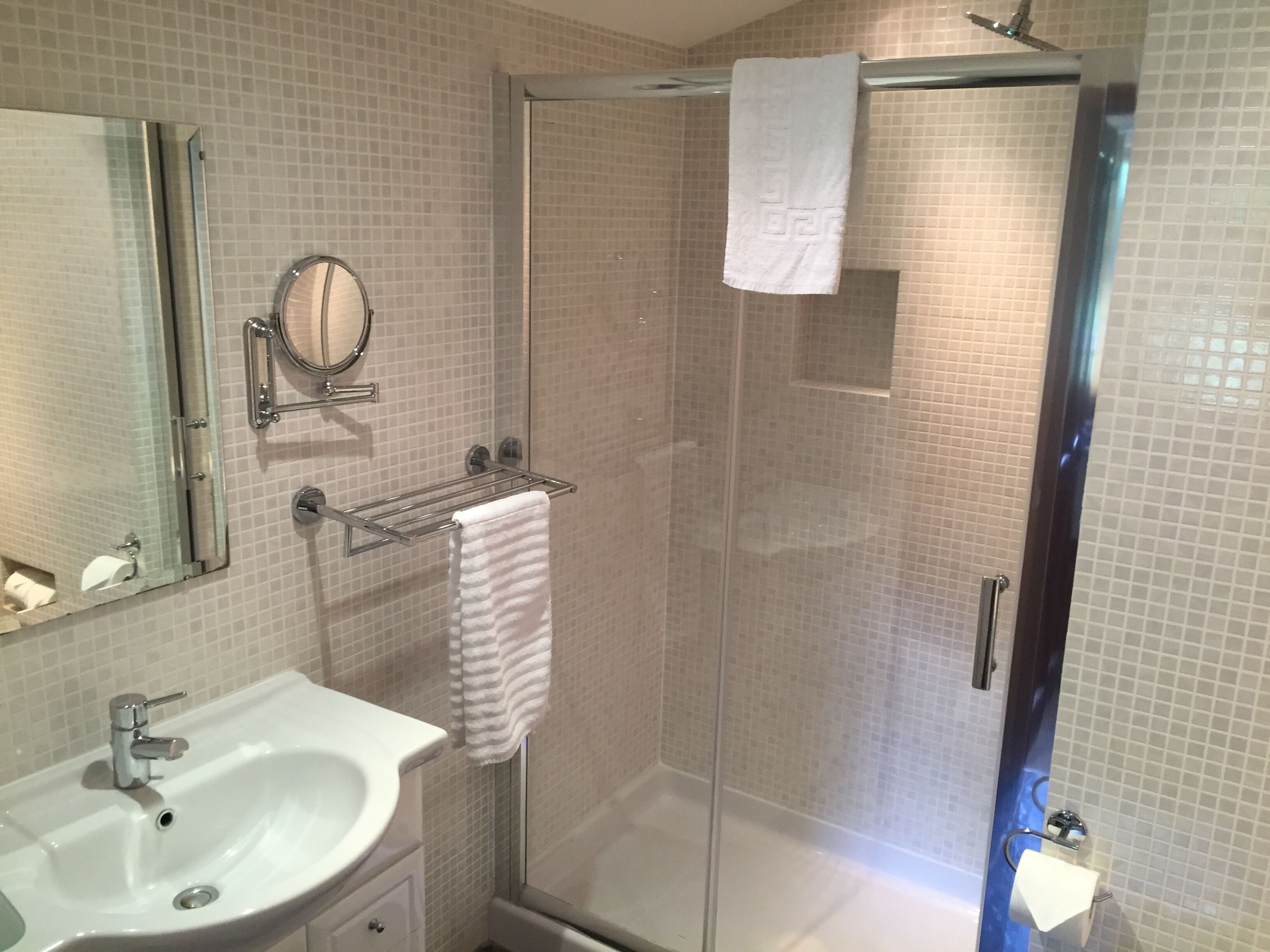 A bathroom with a sink, mirror, towel rack, and a glass shower enclosure.