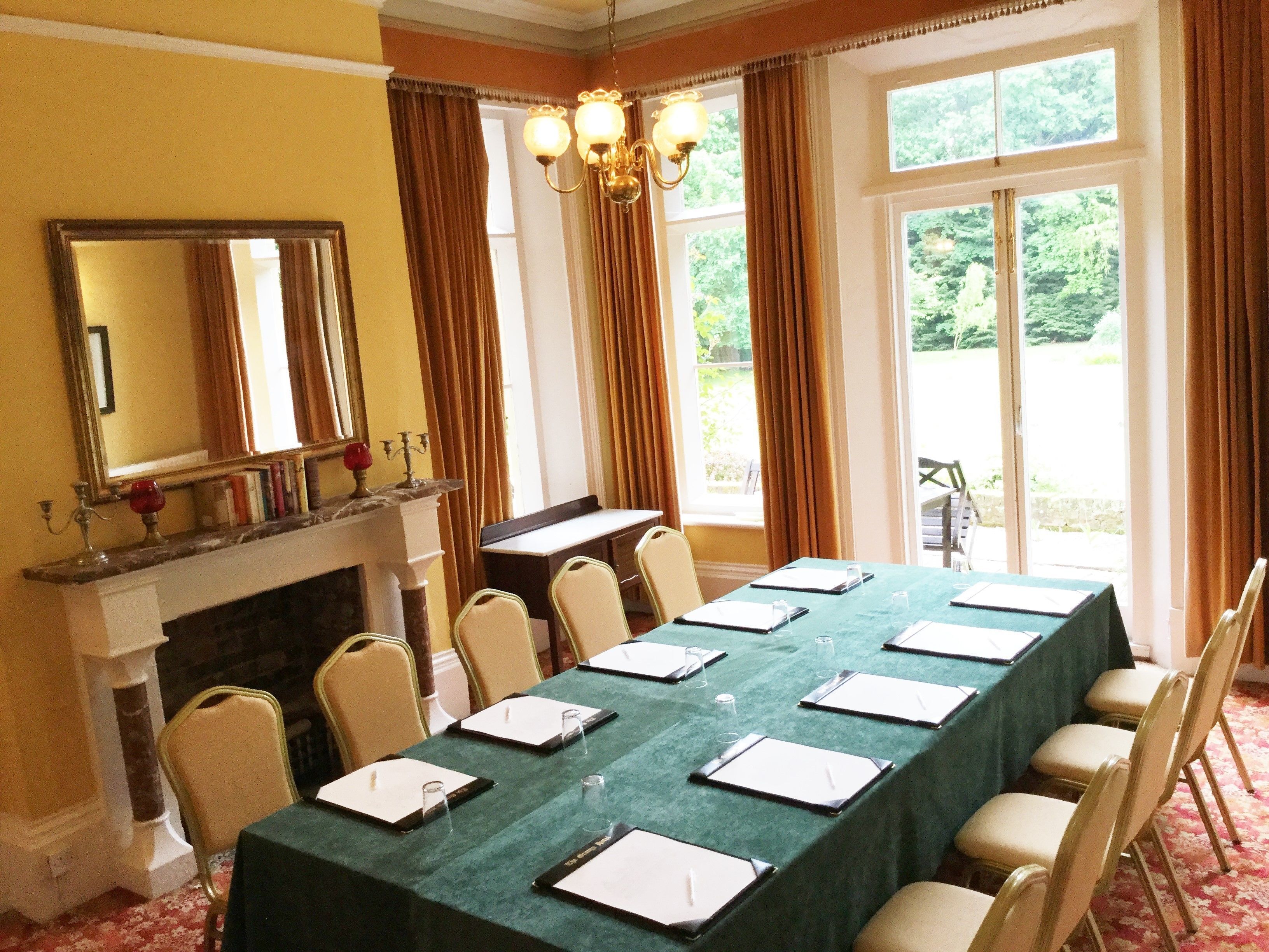 Un salón de conferencias con una larga mesa, sillas, una chimenea y amplios ventanales con cortinas.