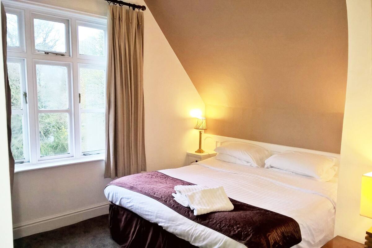 Een slaapkamer met een groot bed, een raam met gordijnen en twee bedlampjes.