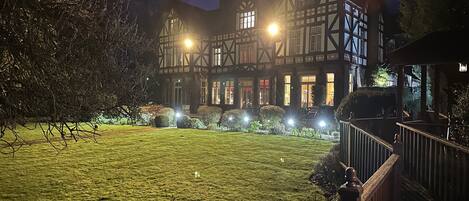 A traditional Tudor-style building with a well-lit garden and a wooden fence.