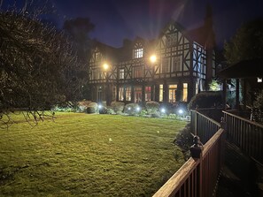 Un edificio de estilo Tudor tradicional con un jardín bien iluminado y una cerca de madera.