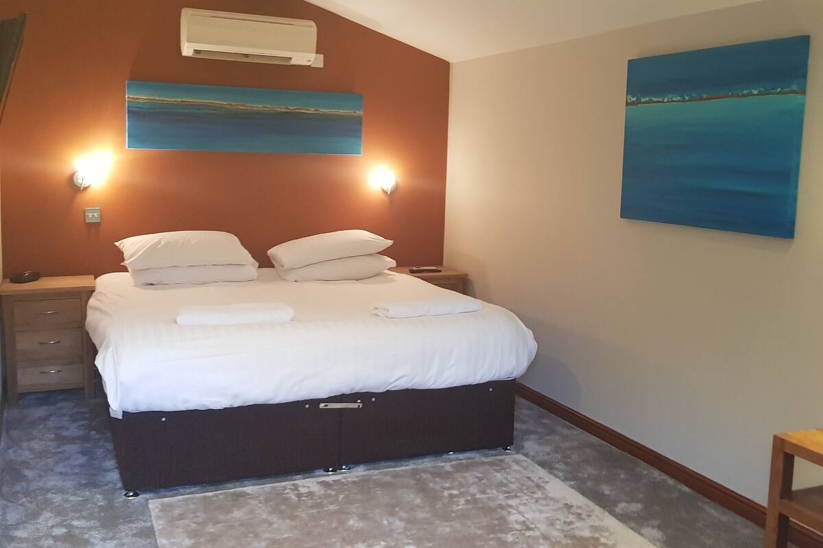 Een slaapkamer met een bed, nachtkastjes, een schilderij en een plafondventilator.