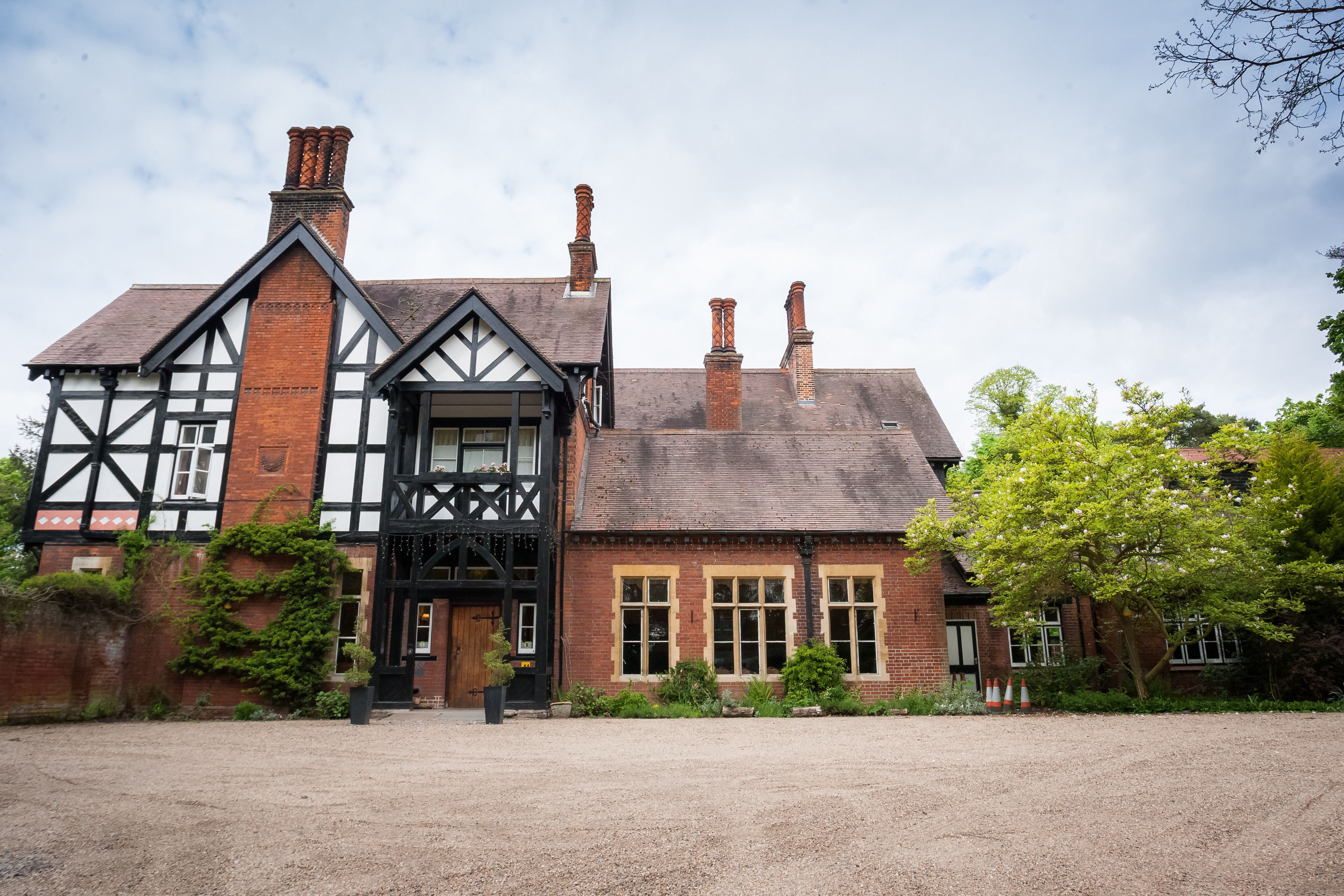 A traditional Tudor-style building with a prominent black and white timber frame, multiple chimneys, and a gravel driveway.