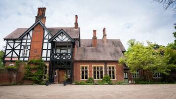 A traditional Tudor-style building with a prominent black and white timber frame, multiple chimneys, and a gravel driveway.