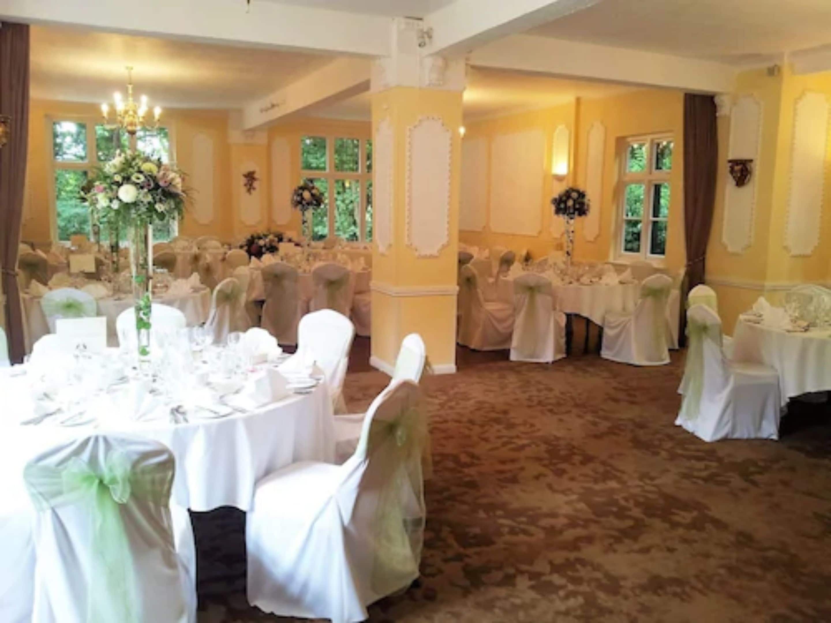A banquet hall with round tables, white chairs, and floral centerpieces.