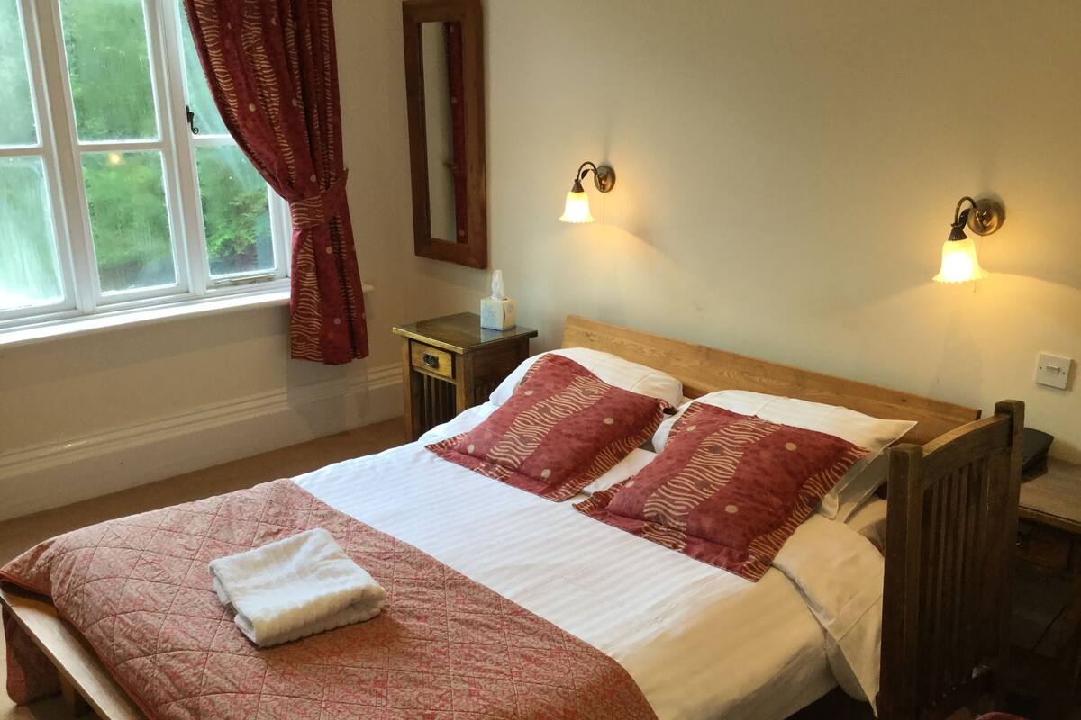 Een net opgemaakt bed met een quilt in rood en wit, een houten hoofdbord en twee wandlampen.
