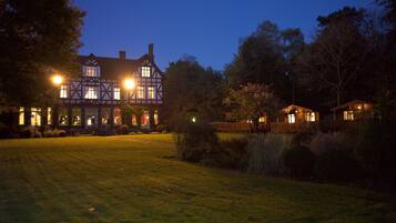 Un gran edificio de estilo Tudor con múltiples ventanas y un césped bien iluminado.