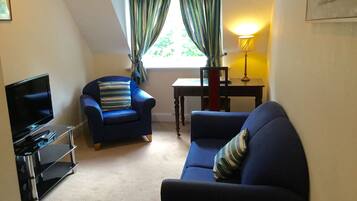 A living room with a TV, two blue sofas, a small table, and a lamp.