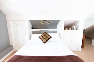 A bedroom with a bed, white wardrobe, and a small kitchenette area with a kettle.
