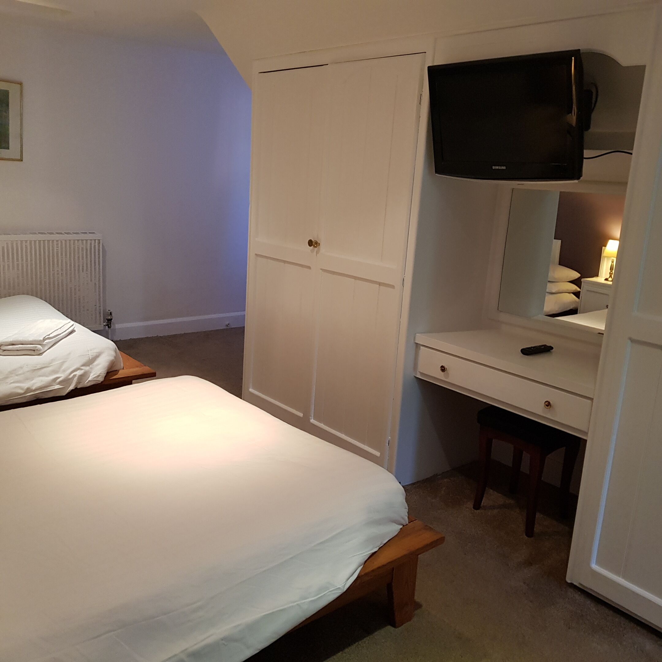 Un dormitorio con una cama, un escritorio con silla, un armario y un televisor sobre el escritorio.
