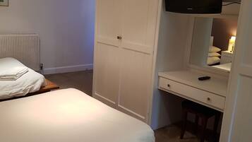 Un dormitorio con una cama, un escritorio con silla, un armario y un televisor sobre el escritorio.