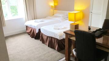 Una habitación de hotel con dos camas, un escritorio con lámpara y una silla.