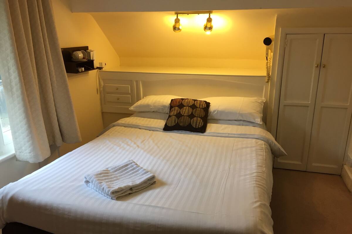 Een net opgemaakt bed met een gevouwen handdoek, een gestreept kussen en een nachtkastje met een lamp.