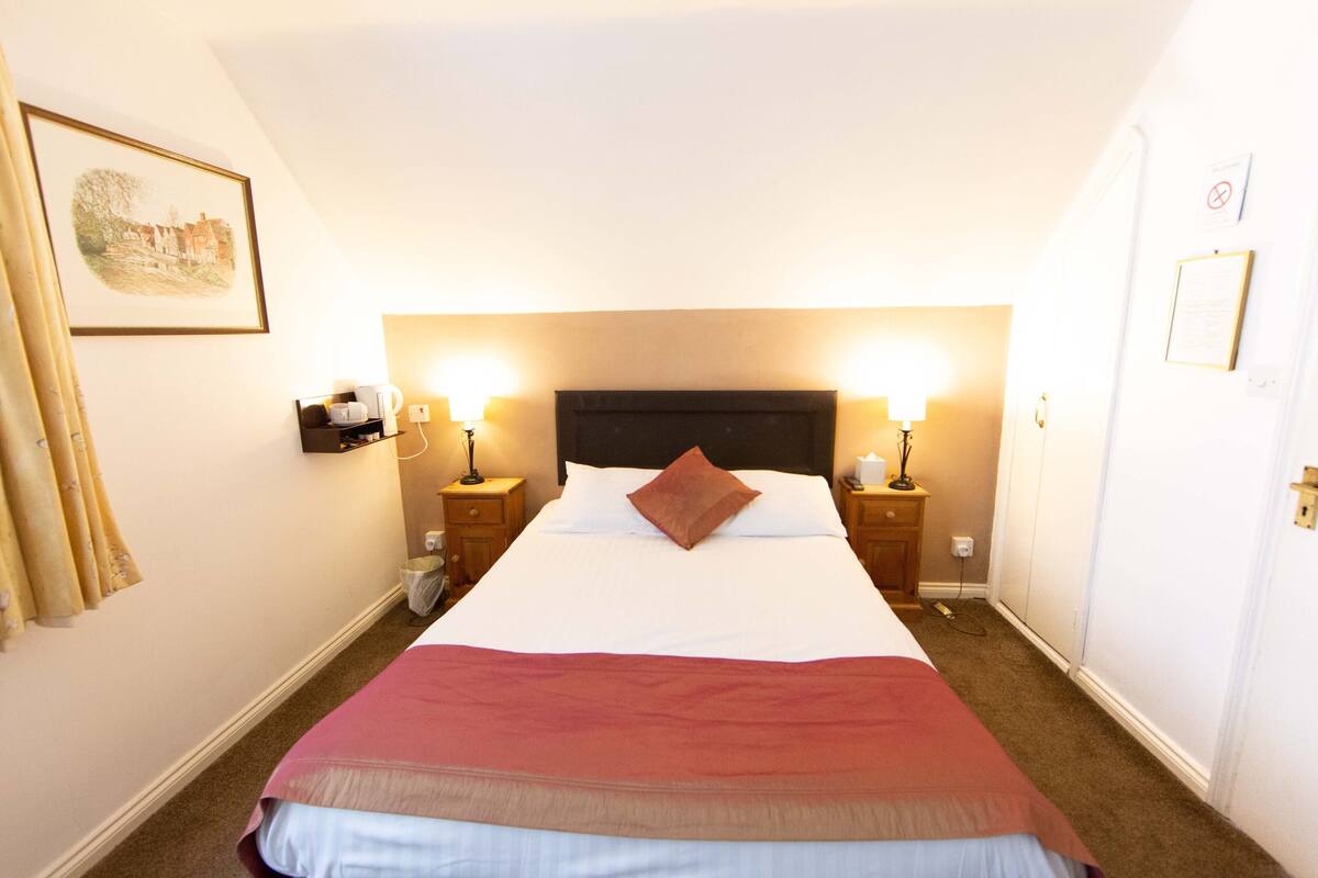 Hotelkamer met groot bed, twee nachtkastjes met lampen, hoofdeinde, een ingelijst kunstwerk aan de muur en een deur met slot.