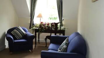 Un salón con dos sillones azules, una mesa de centro de madera y un jarrón con flores, además de una lámpara.