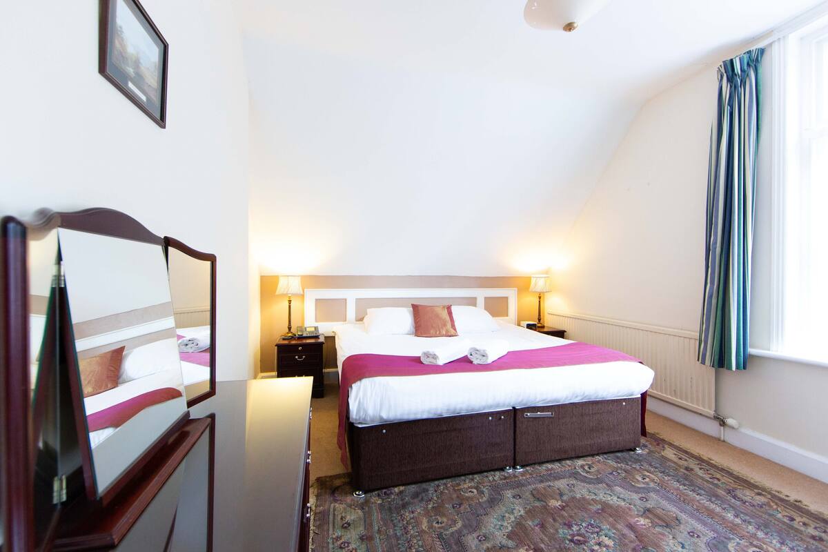 Een slaapkamer met een bed, nachtlampjes, een spiegel en een raam met gordijnen.