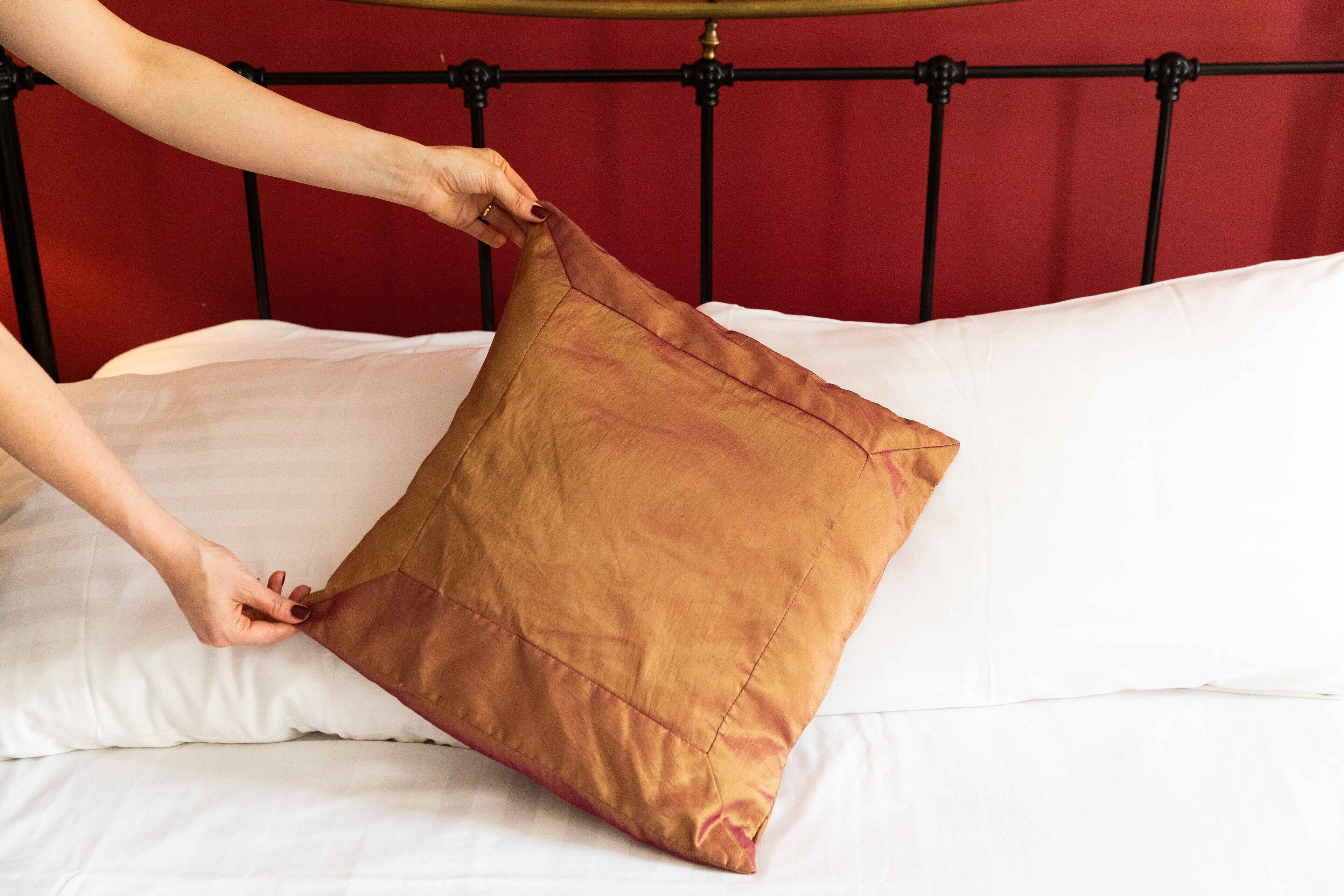 A hand adjusting a brown pillow on a bed with a red headboard.