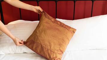 A hand adjusting a brown pillow on a bed with a red headboard.