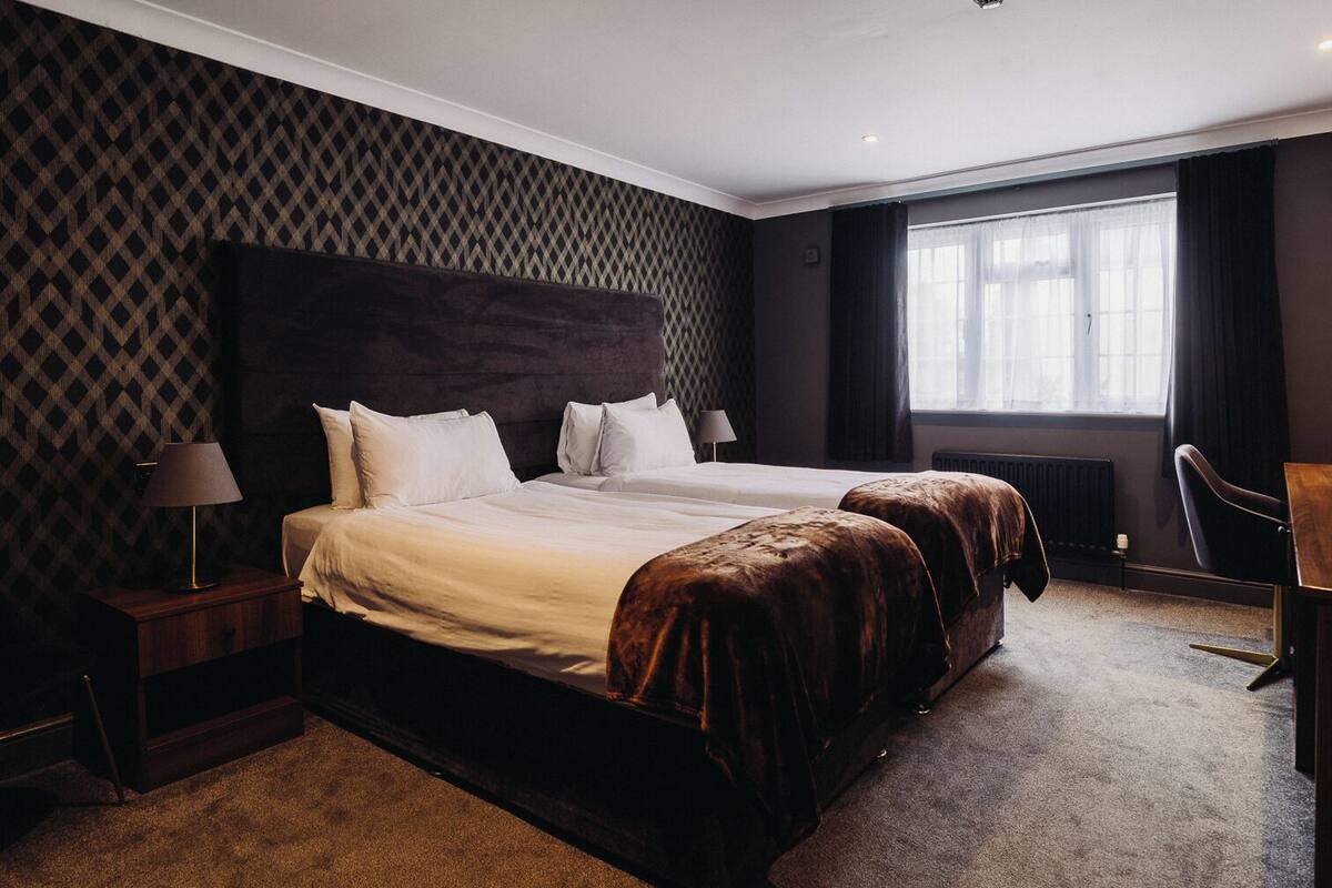 A hotel room with a large bed, two bedside tables, a chair, and a window with curtains.
