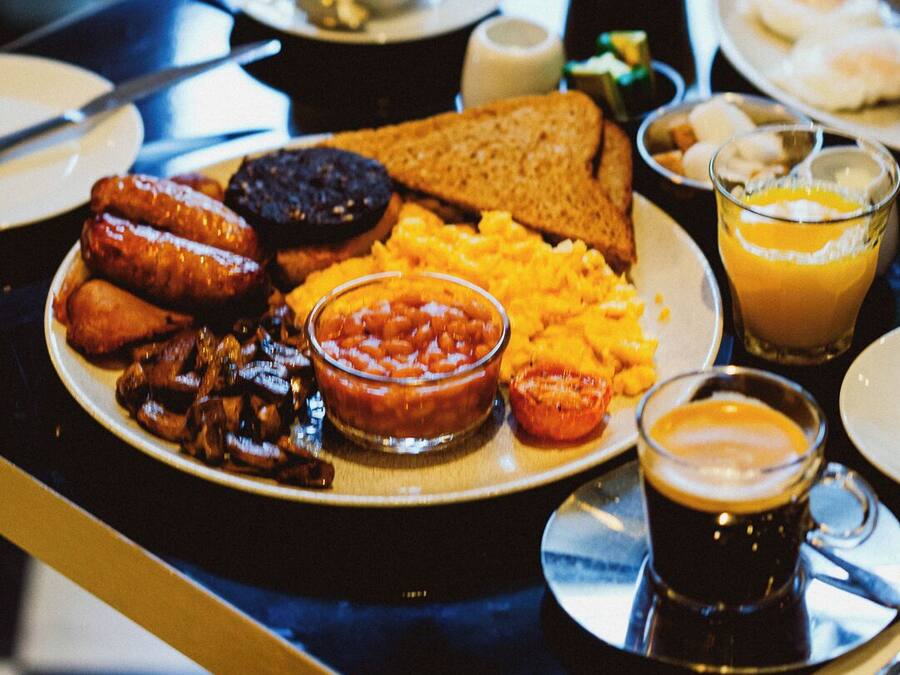 A breakfast table with plates of food, including toast, sausages, beans, scrambled eggs, and a glass of orange juice.