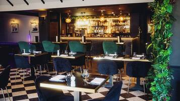 A restaurant with checkered flooring, green upholstered chairs, and a bar area with a variety of bottles and glasses.