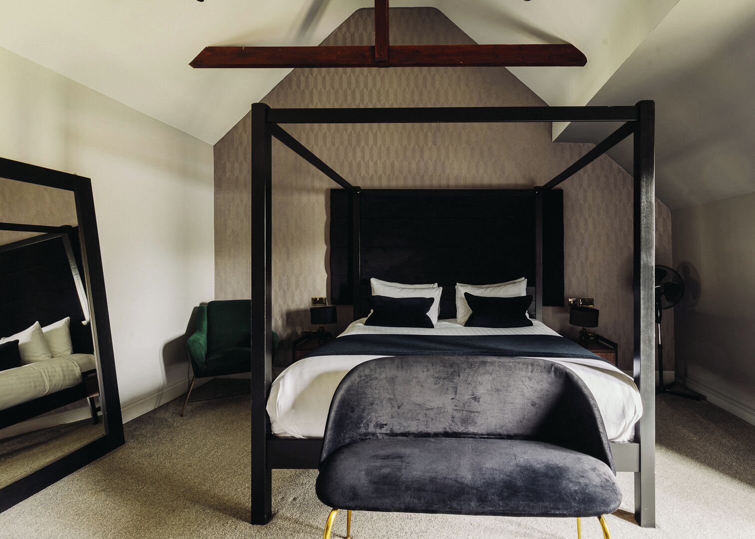 Una cama con dosel, un cabecero oscuro, un sillón verde y un banco tapizado en negro.
