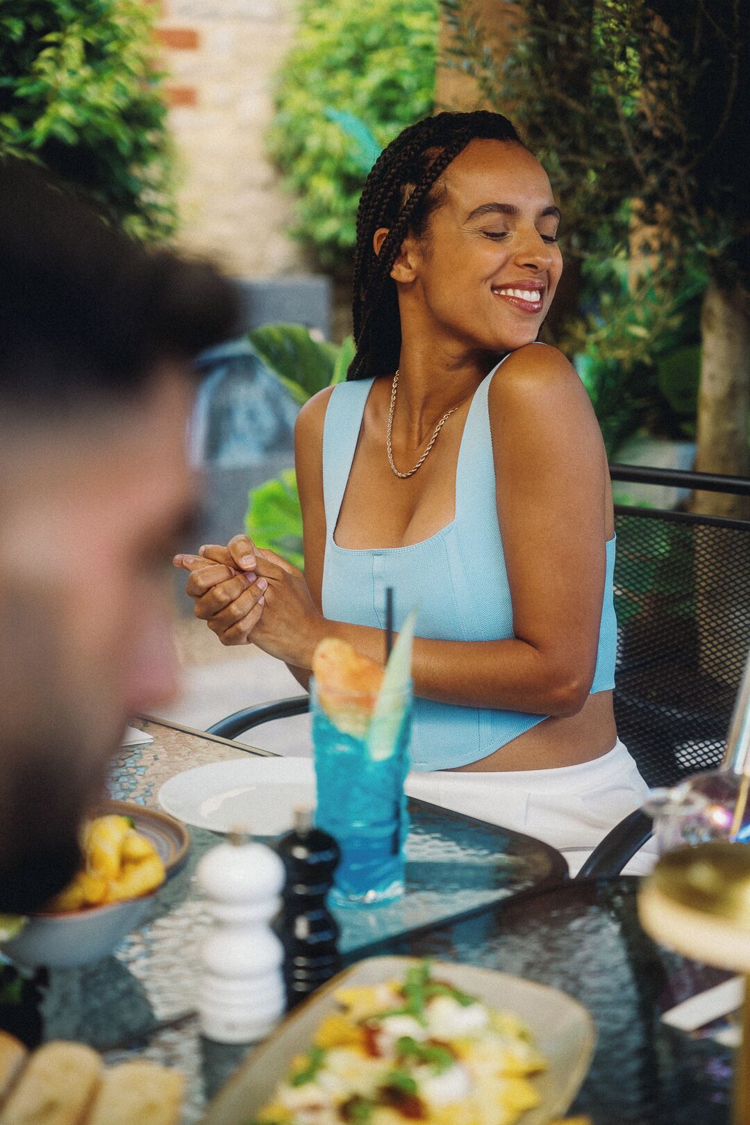 Una persona sentada en una mesa al aire libre, con una bebida y alimentos.