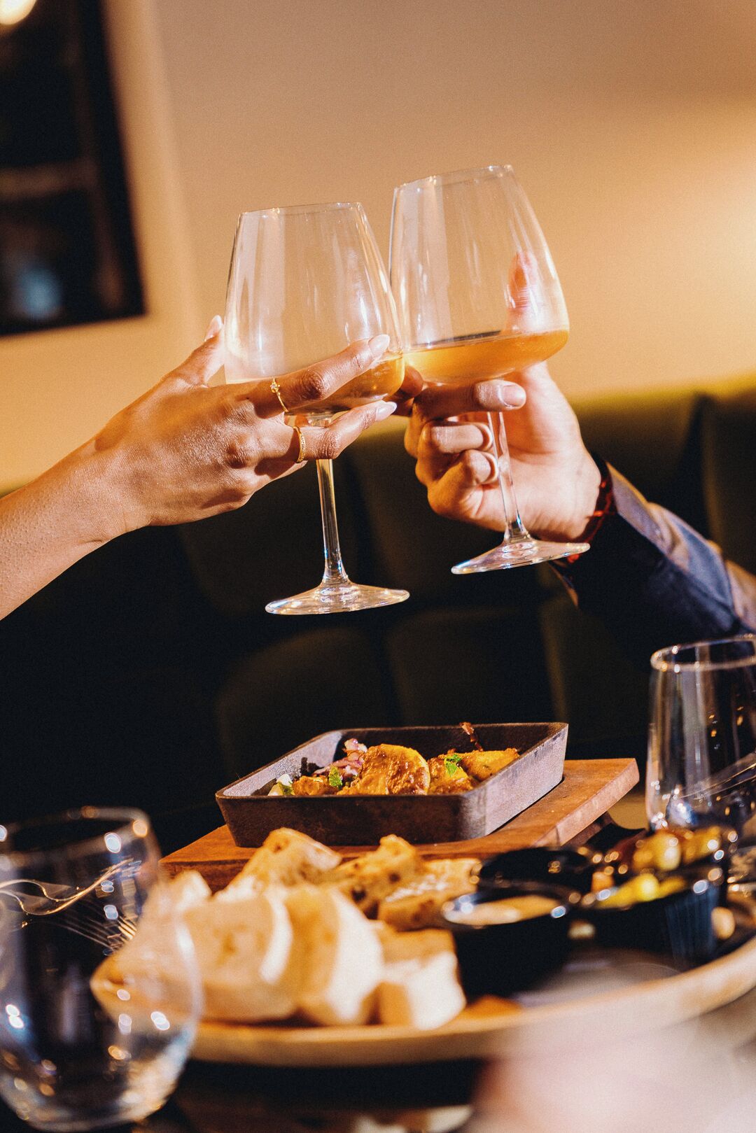Two people toasting with wine glasses, a tray of food, and a dessert plate.