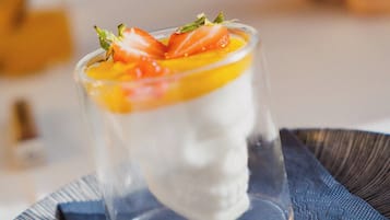 Un postre en un vaso transparente sobre un plato con un mantelito azul debajo.