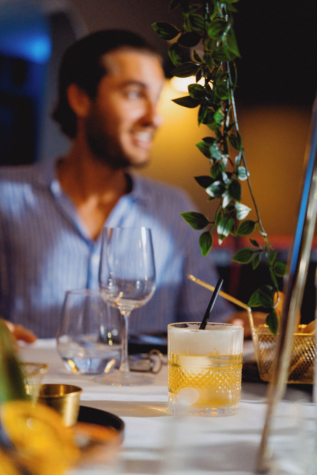 A dining table with a glass of a yellow beverage, a wine glass, and a gold-colored container.