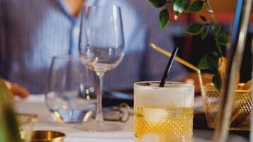 A dining table with a glass of a yellow beverage, a wine glass, and a gold-colored container.