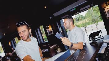 Two men at a bar with a view of greenery outside.