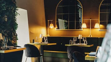 Interior de un restaurante con suelo a cuadros, sillas de tonos oscuros y mesas dispuestas con copas de vino y cubiertos.