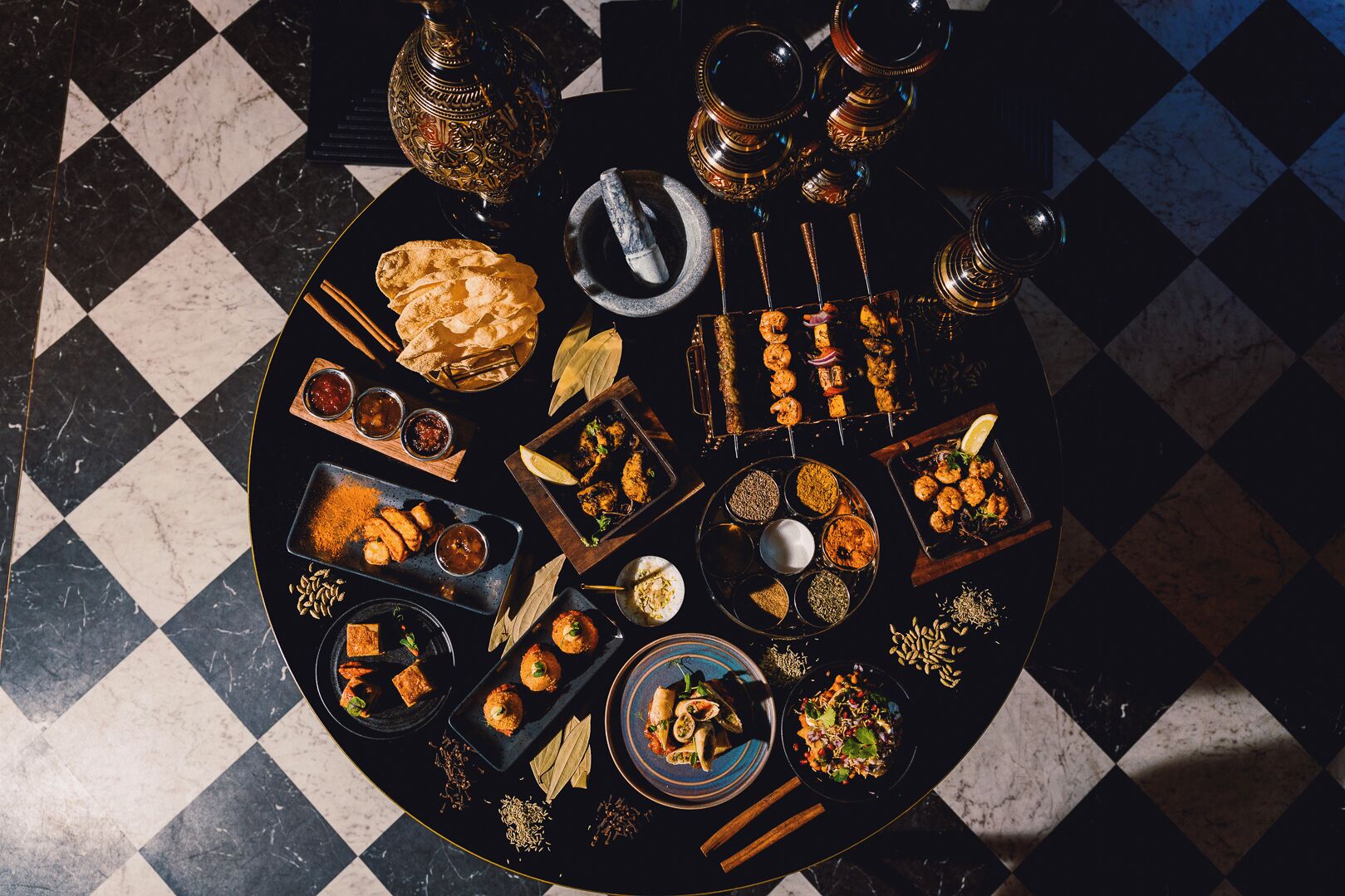 A round table with various dishes and drinks, surrounded by a checkered floor.