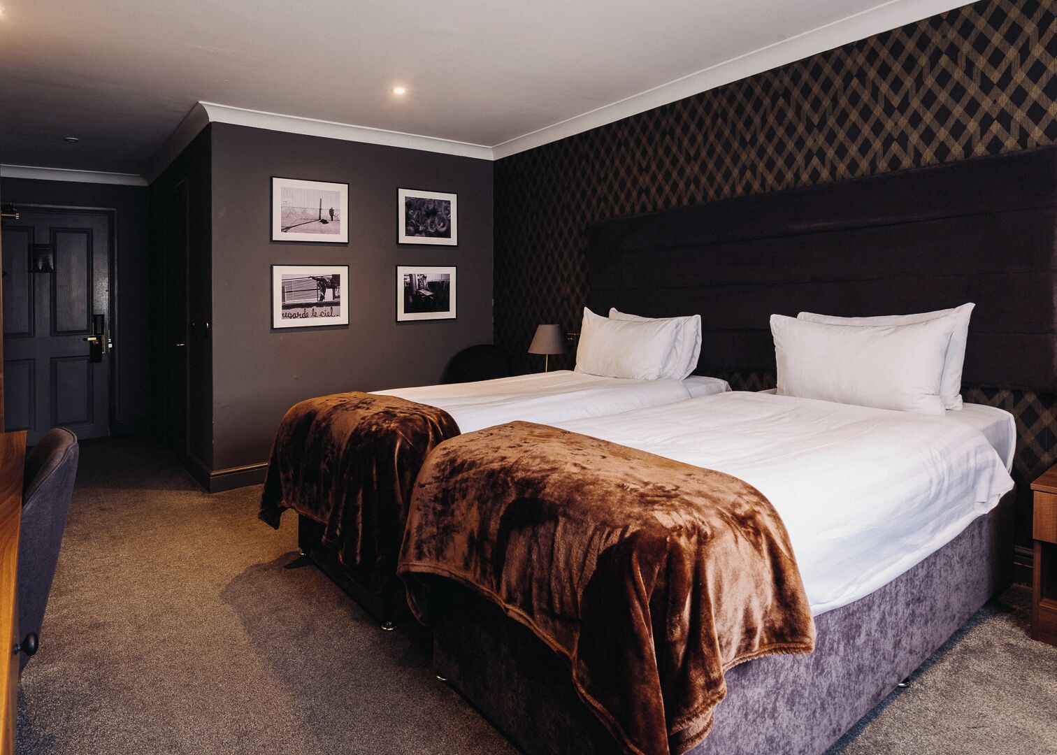A hotel room with two beds, a dark patterned headboard, and a carpeted floor.