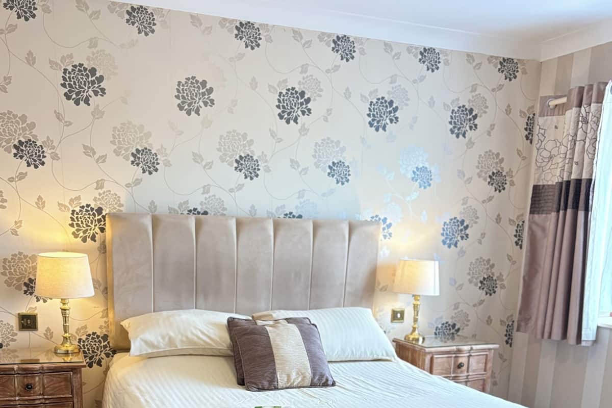 A neatly made bed with white linens, a headboard, and two bedside lamps.