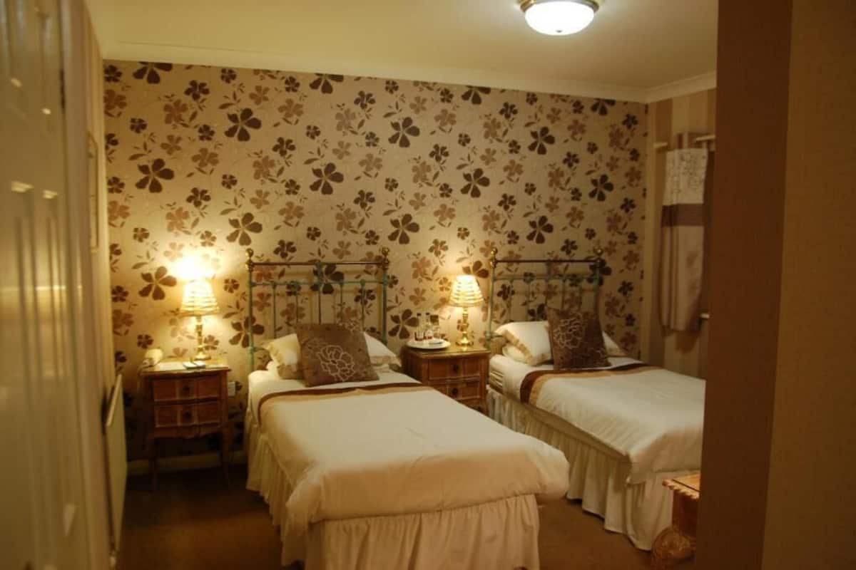 A hotel room with two beds, floral wallpaper, bedside lamps, and a wooden nightstand.