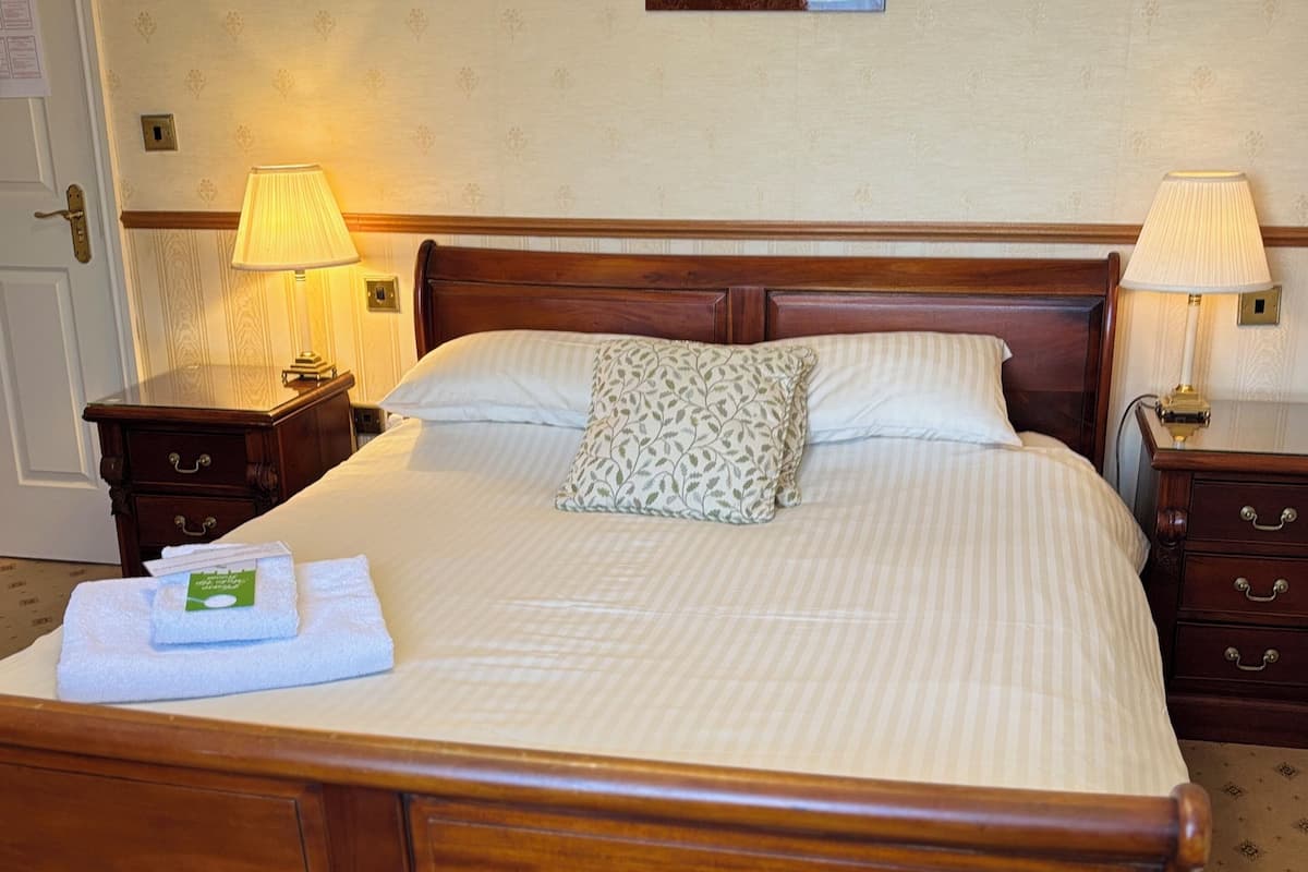 A neatly made bed with a wooden headboard, two bedside tables with lamps, a framed picture on the wall, and a door to the left.