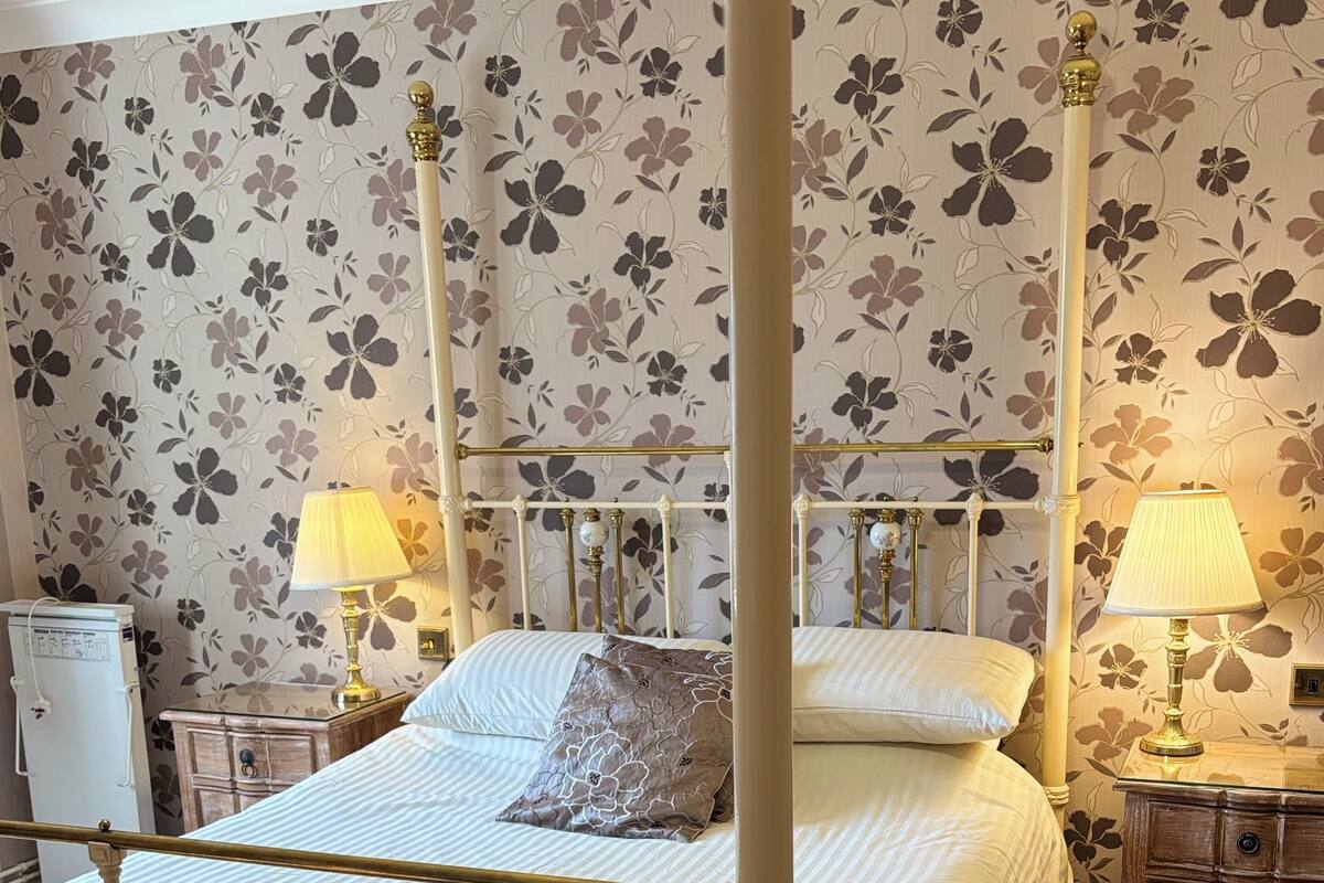A four-poster bed with a white and gold frame, a white bedspread, and two bedside lamps.