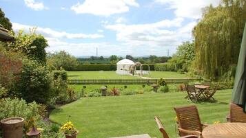 A garden with a gazebo, a lawn, and a patio with chairs and a table.