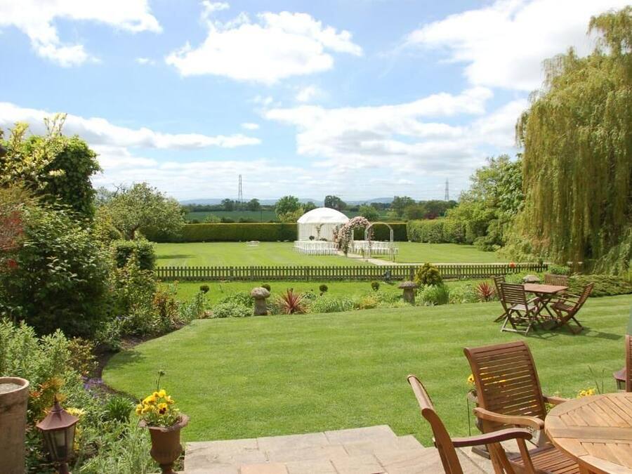 A garden with a gazebo, a lawn, and a patio with chairs and a table.