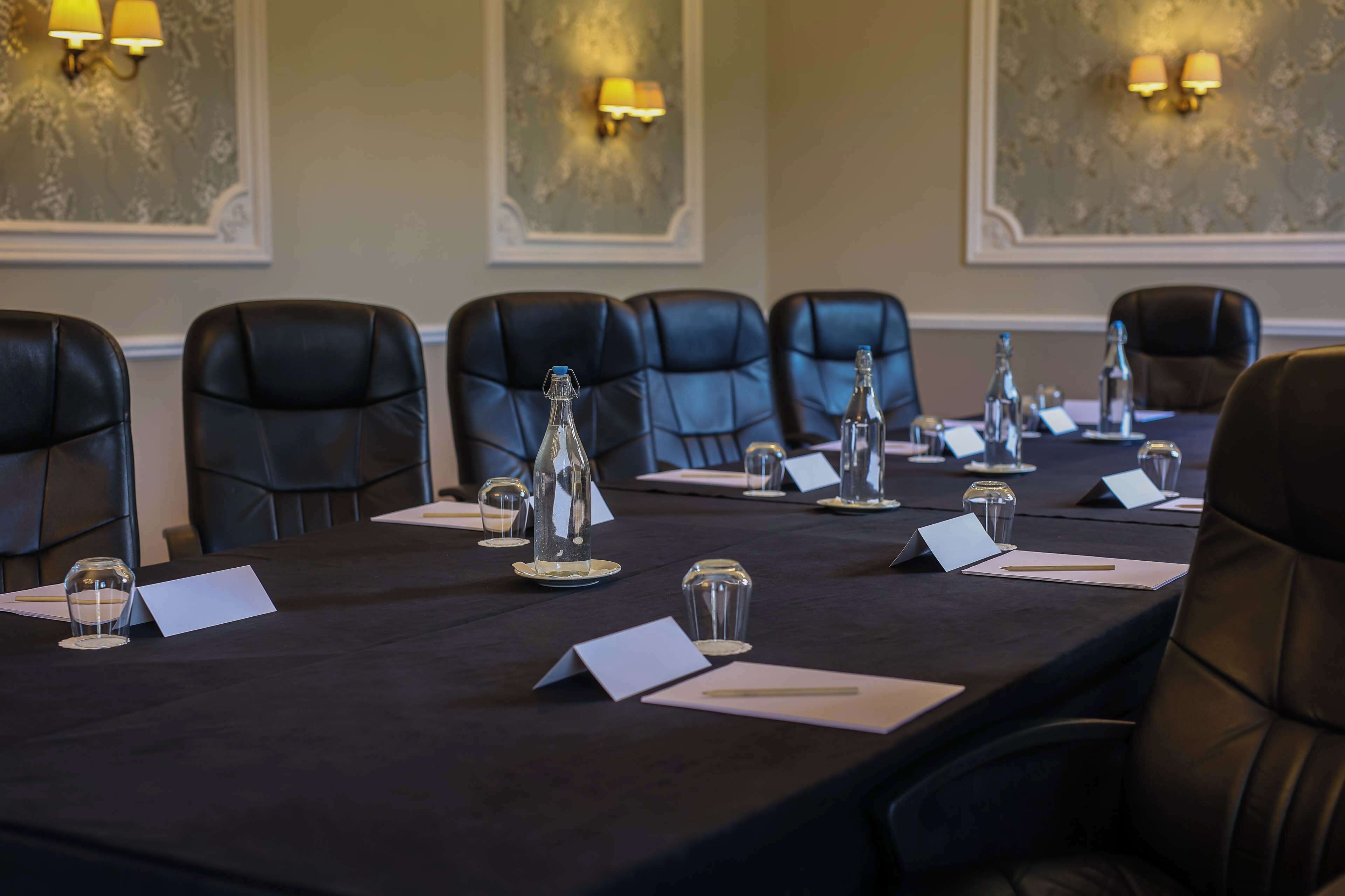 A conference room with a long table, black leather chairs, name cards, water glasses, and a bottle of water.