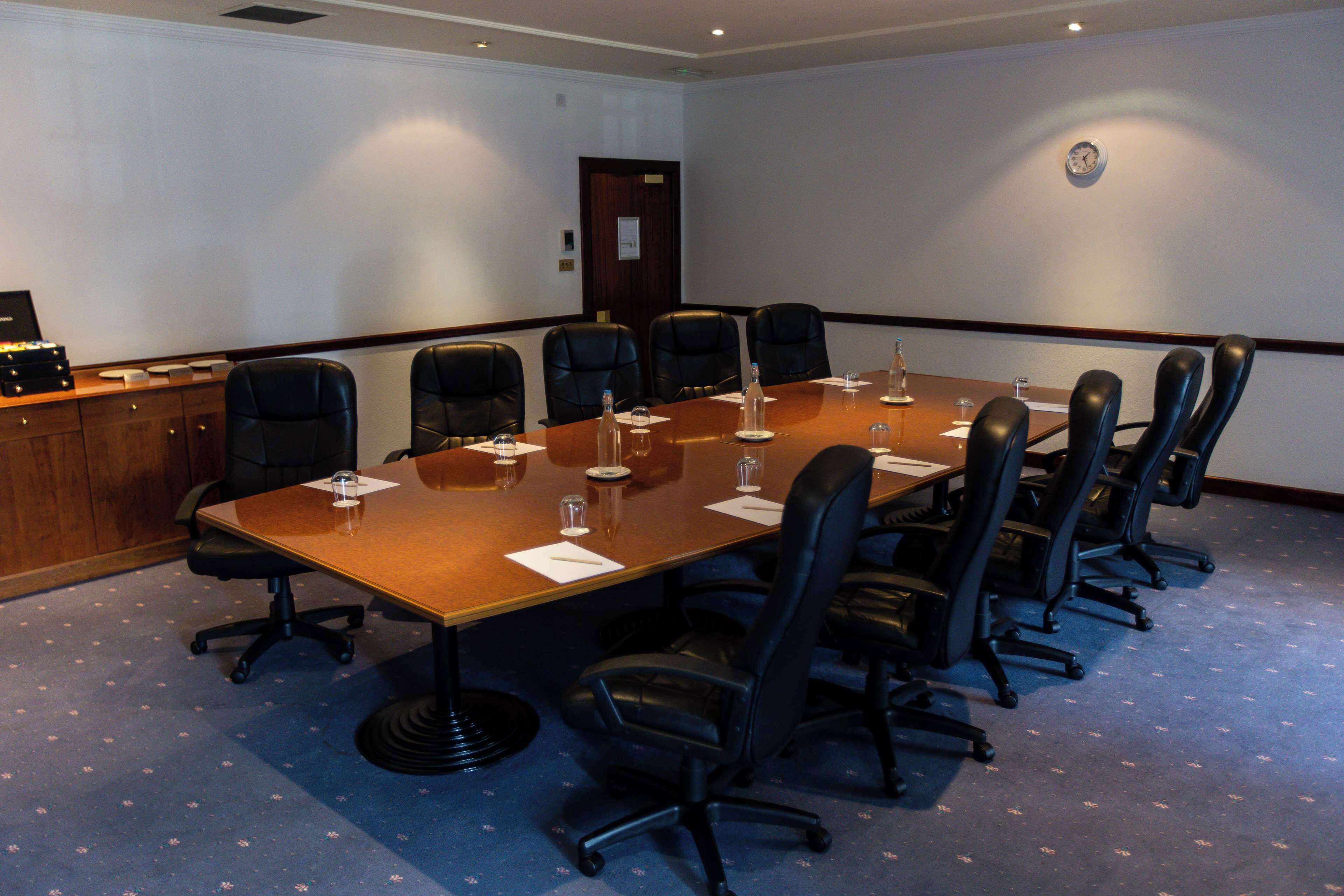 A conference room with a long table, black chairs, and a wooden paneling wall.