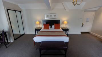 A hotel room with a large bed, two bedside tables with lamps, a bench at the foot of the bed, a door, and a framed picture on the wall.