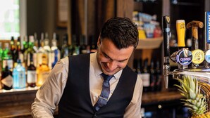 Un cantiner preparant begudes al bar, amb una varietat de botelles i gots de coure.