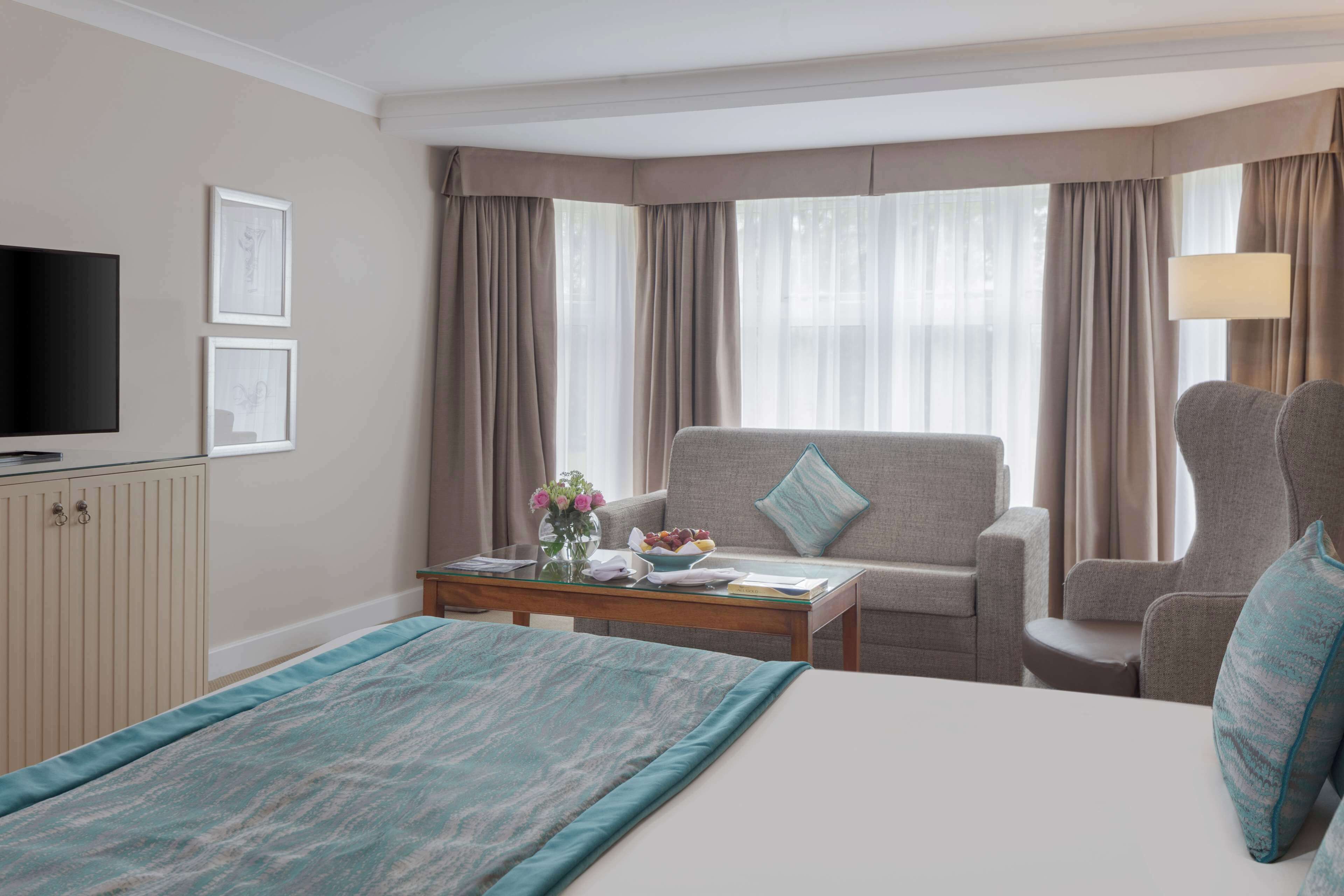 Una habitación de hotel con cama, sofá, televisor y ventana con cortinas.