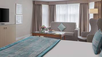 Una habitación de hotel con cama, sofá, televisor y ventana con cortinas.