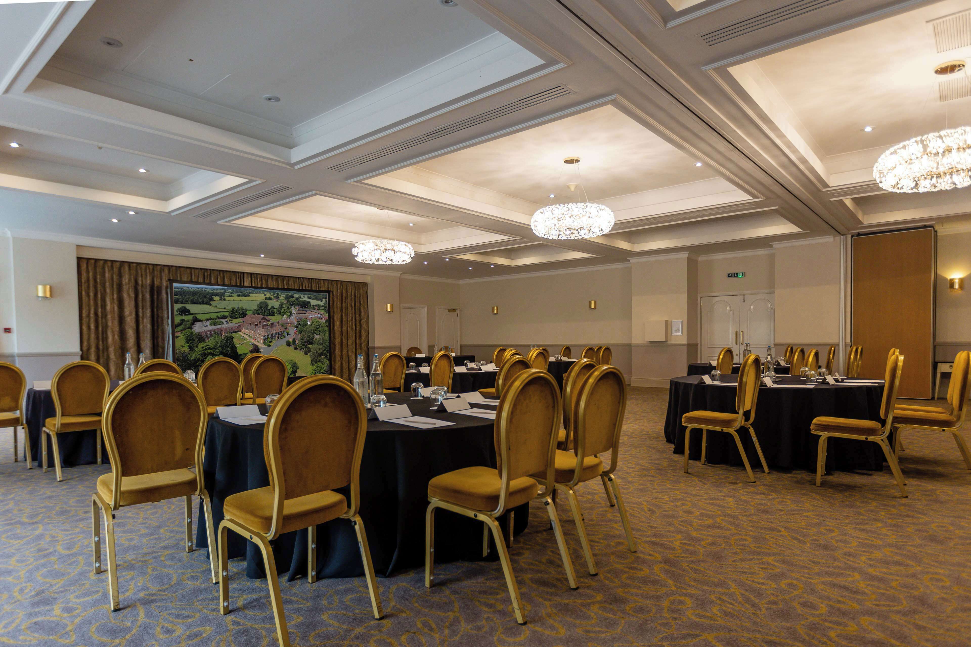 A conference room with round tables, gold chairs, and chandeliers.